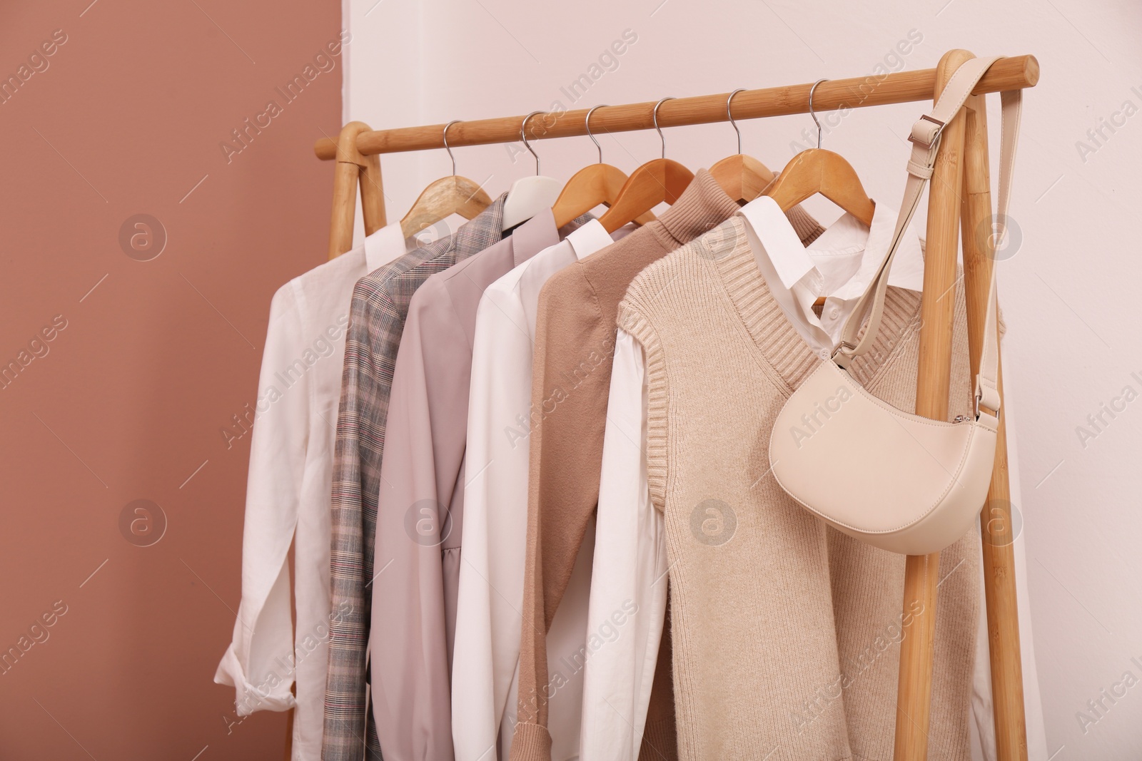 Photo of Rack with different stylish clothes and bag near white wall indoors