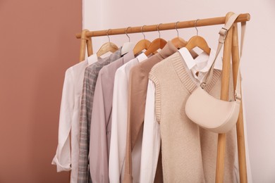 Rack with different stylish clothes and bag near white wall indoors