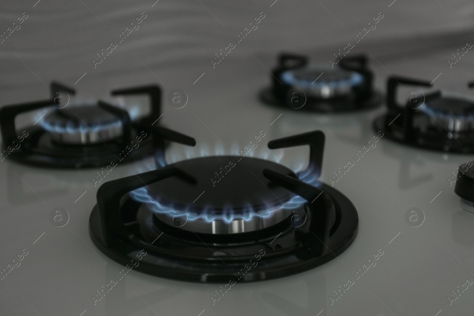 Photo of Gas burners with blue flame on modern stove. Space for text