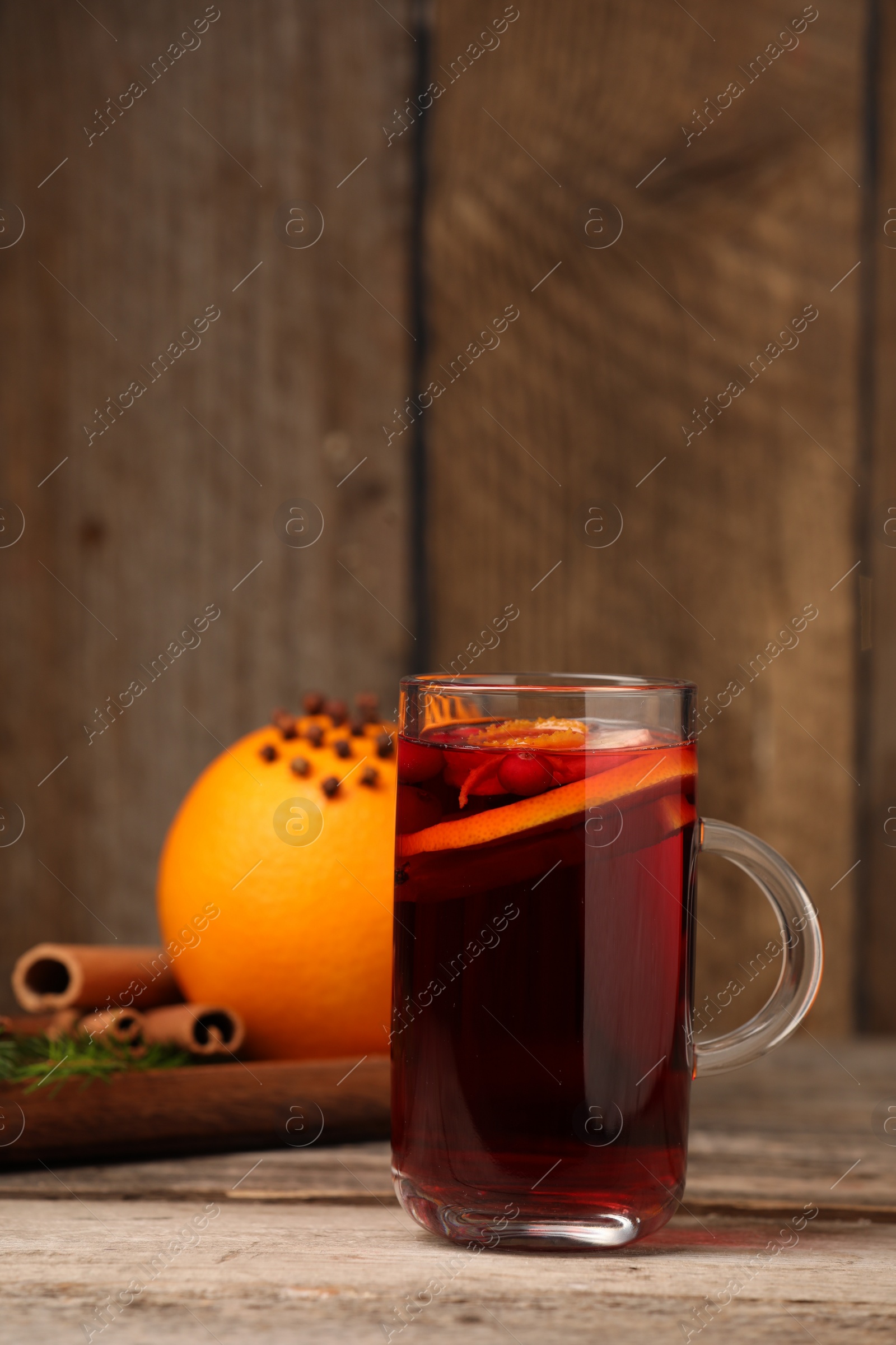 Photo of Aromatic mulled wine in glass cup on wooden table, space for text