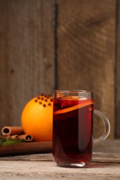 Aromatic mulled wine in glass cup on wooden table, space for text