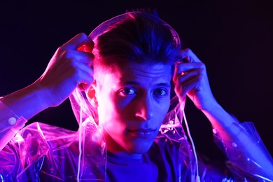 Photo of Young man wearing clear coat on dark background in neon lights