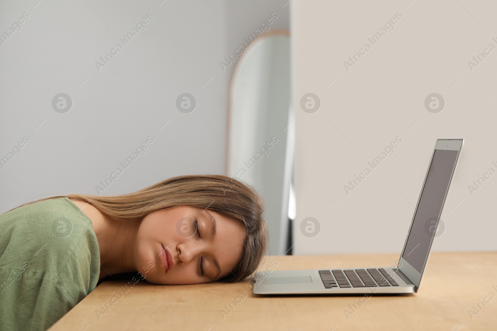 Photo of Young woman sleeping in front of laptop at wooden table indoors