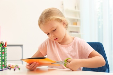 Photo of Little left-handed girl cutting construction paper at table