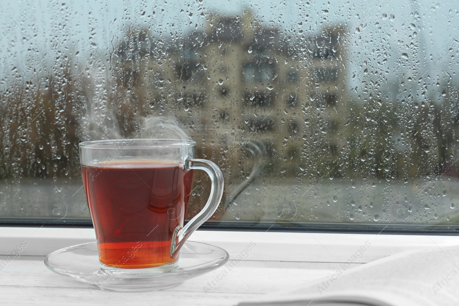 Photo of Glass cup of tea on windowsill, space for text. Rainy weather