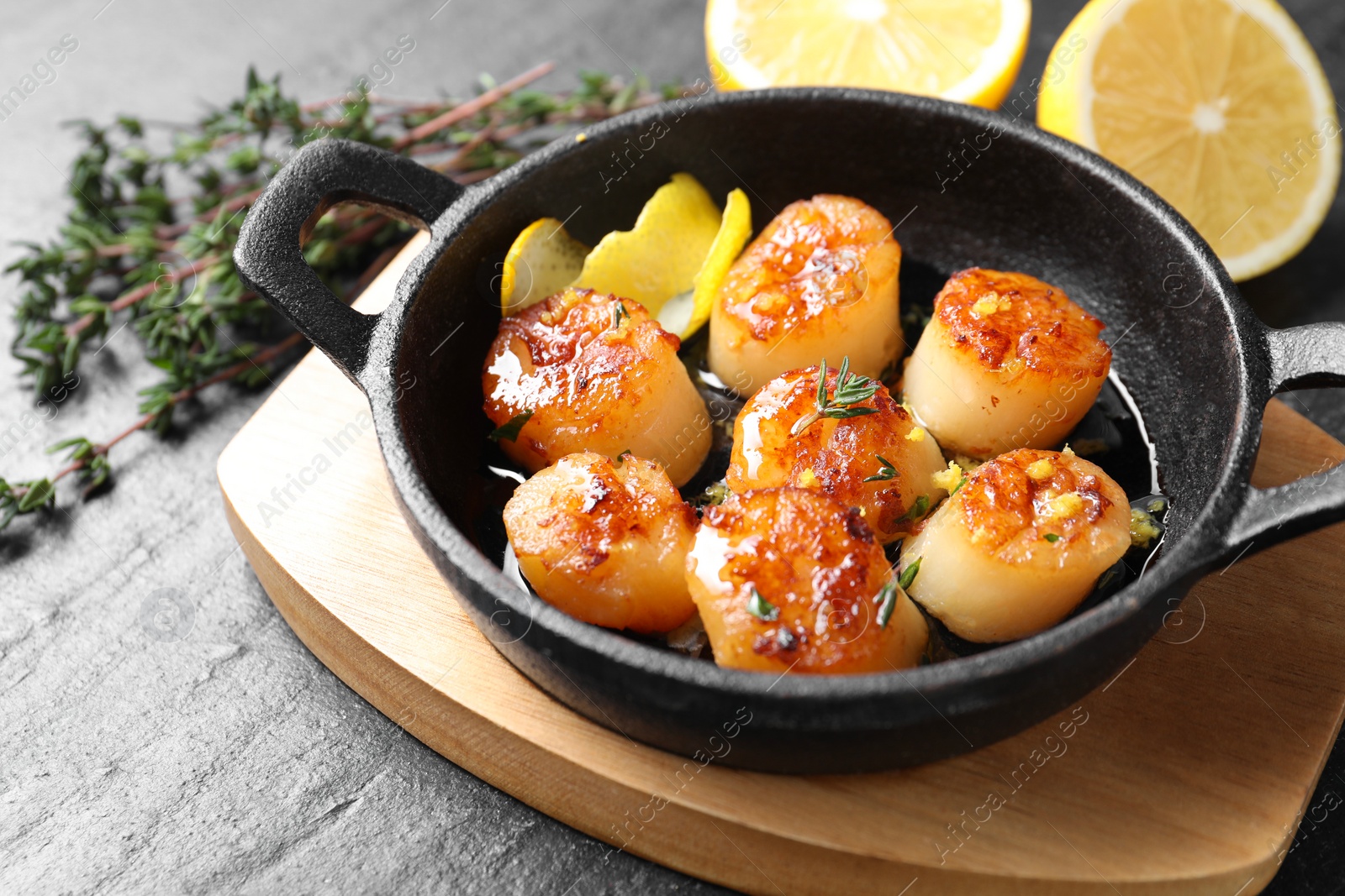 Photo of Delicious fried scallops and ingredients on dark gray textured table, closeup