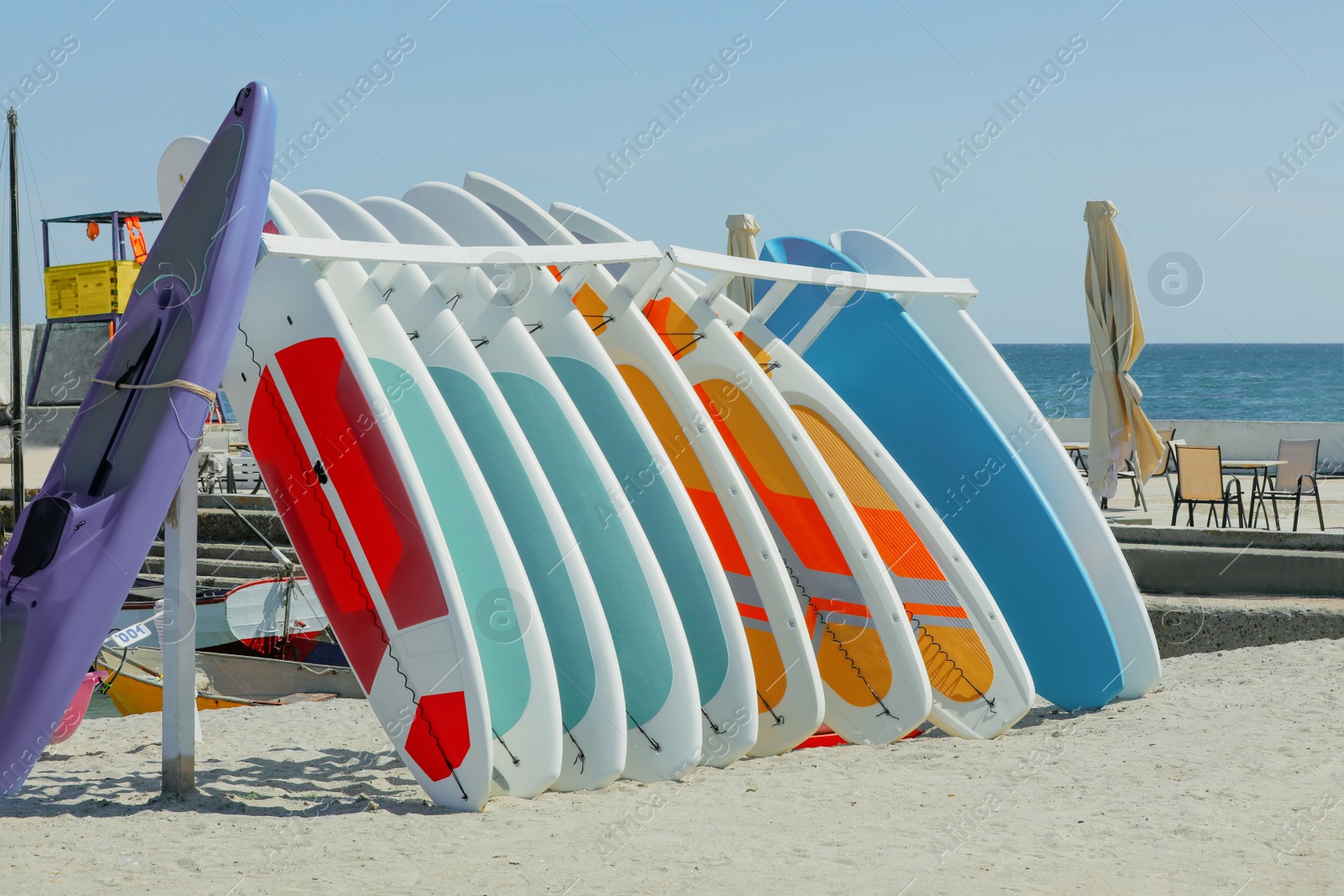 Photo of Holder with colorful paddle boards and kayak on sand near sea