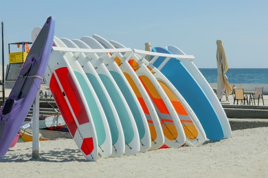 Holder with colorful paddle boards and kayak on sand near sea