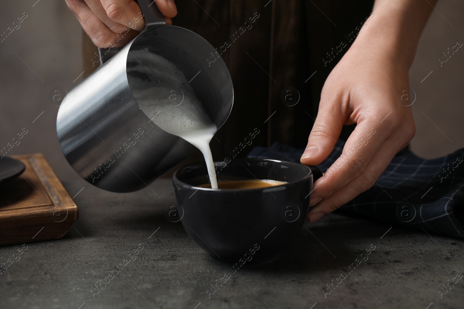 Photo of Woman pouring milk into cup of coffee at grey table, closeup