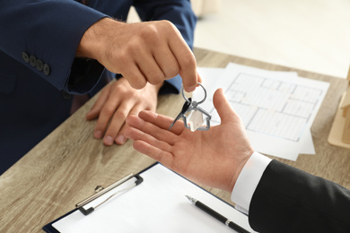 Real estate agent giving key to client at table in office, closeup