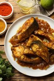 Photo of Tasty Indian fish curry on wooden table, flat lay