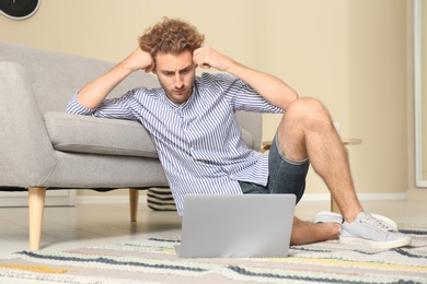 Photo of Young man with laptop sitting on floor at home