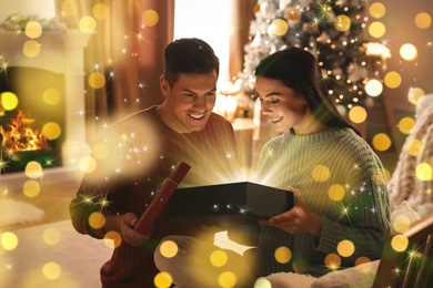 Image of Couple opening Christmas gift with magic light at home. Bokeh effect