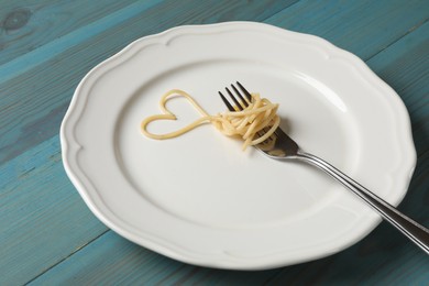 Photo of Heart made of tasty spaghetti and fork on light blue wooden table