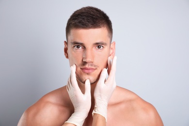 Doctor examining man's face for cosmetic surgery on grey background