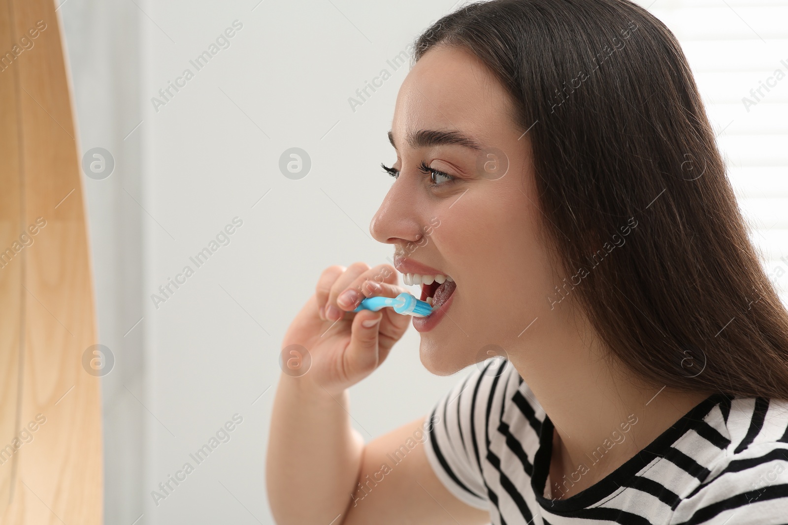 Photo of Young woman brushing her teeth with plastic toothbrush near mirror in bathroom