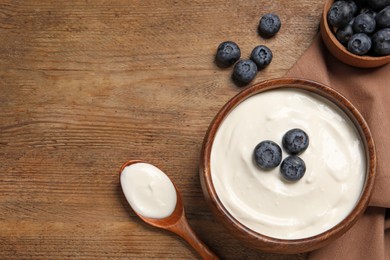 Photo of Bowl of tasty yogurt served with blueberries on wooden table, flat lay. Space for text