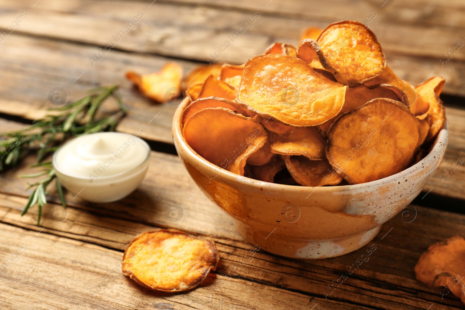 Photo of Delicious sweet potato chips in bowl, rosemary and sauce on table. Space for text