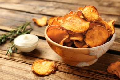 Photo of Delicious sweet potato chips in bowl, rosemary and sauce on table. Space for text