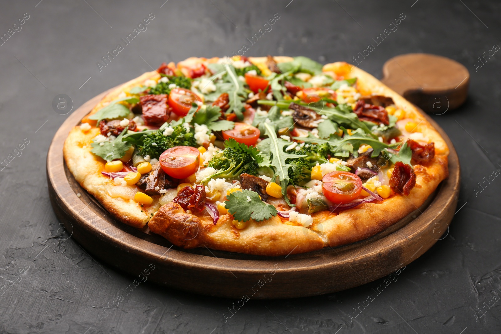 Photo of Delicious vegetarian pizza with cheese, mushrooms, vegetables and greens on black table