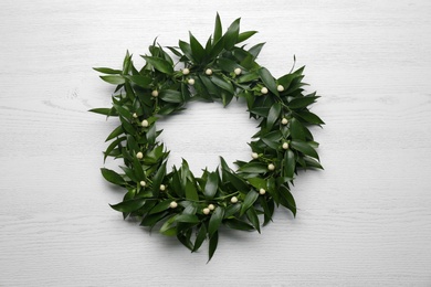 Beautiful handmade mistletoe wreath on white wooden table, top view. Traditional Christmas decor