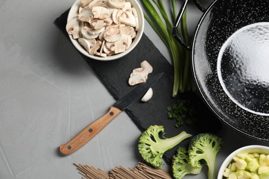 Photo of Wok pan, noodles and different vegetables on light grey table, flat lay. Space for text