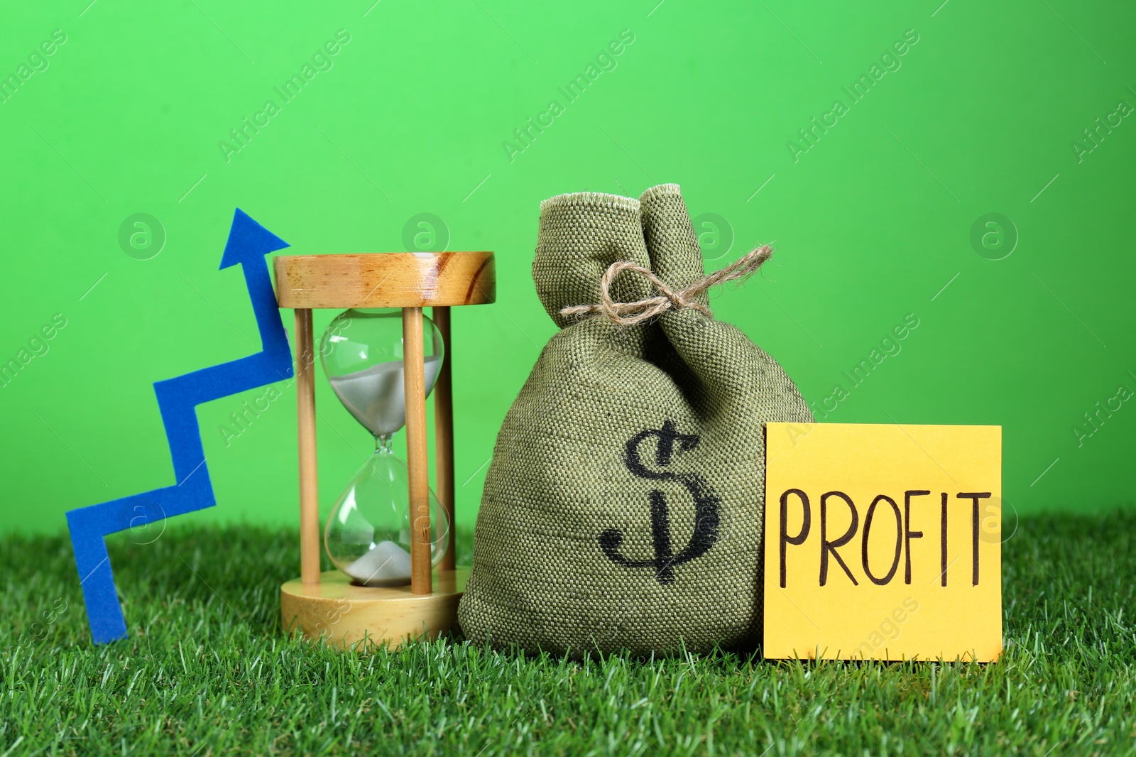 Photo of Sticky note with word Profit, money of bag, up arrow and sandglass against green background