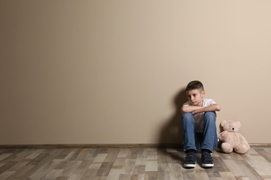 Upset boy with toy sitting on floor at color wall. Space for text