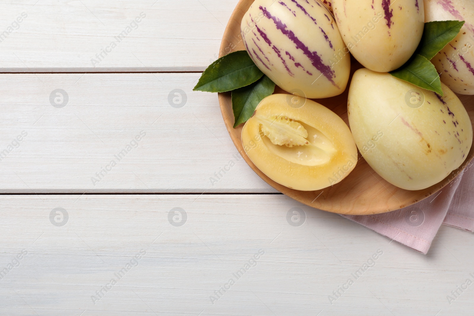 Photo of Whole and cut pepino melons on white wooden table, top view. Space for text