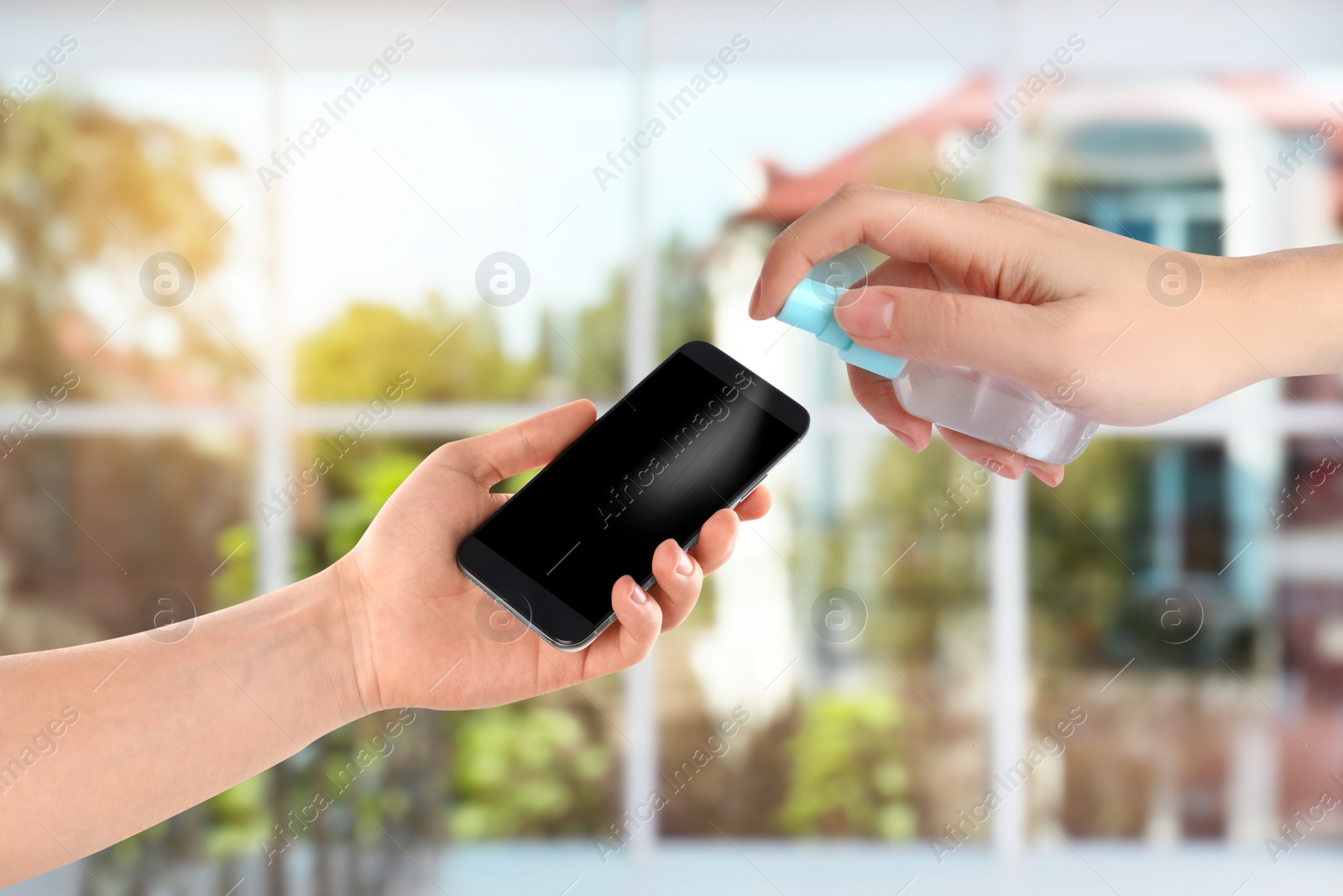 Image of Woman sanitizing smartphone with antiseptic spray indoors, closeup. Be safety during coronavirus outbreak 