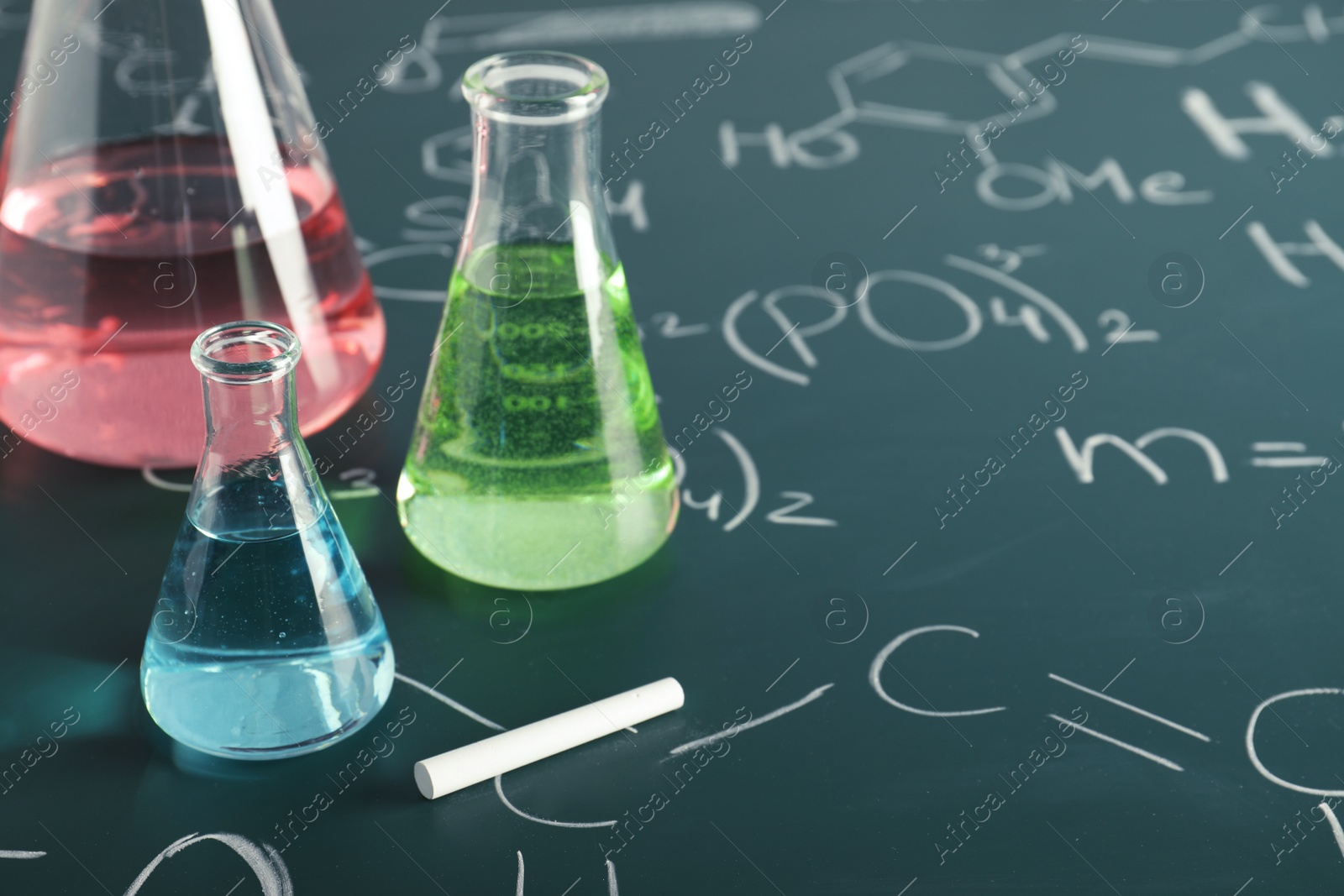 Photo of Laboratory glassware on blackboard with chemical formulas, closeup