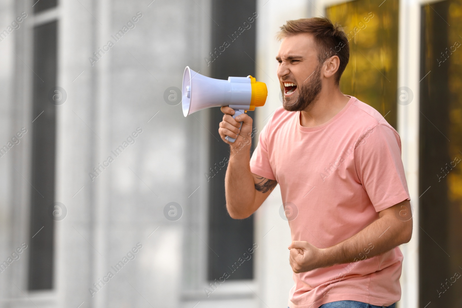 Image of Emotional young man with megaphone outdoors. Protest leader