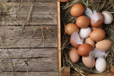 Photo of Fresh chicken eggs and dried hay in crate on wooden table, top view. Space for text