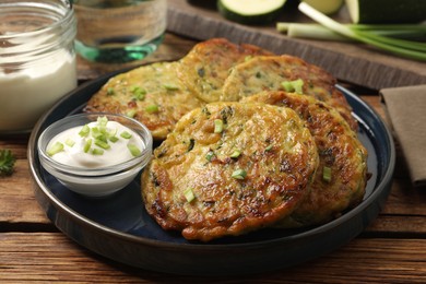 Photo of Delicious zucchini fritters with sour cream served on wooden table