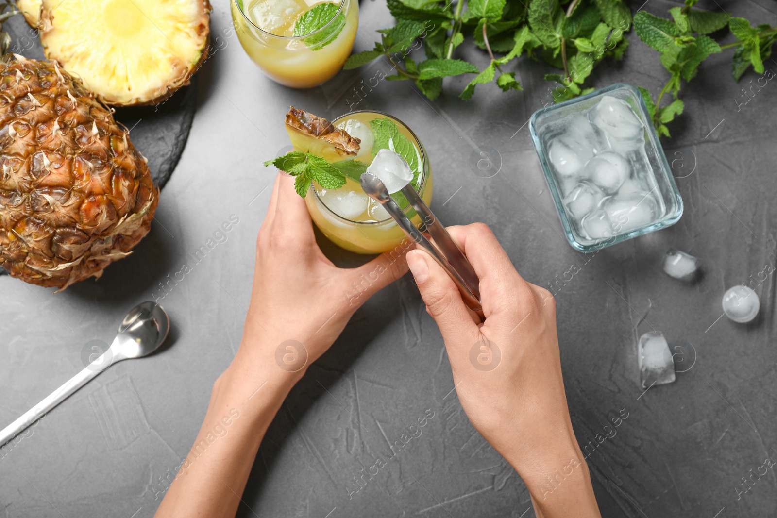 Photo of Woman putting ice in glass with cocktail  at grey table, top view