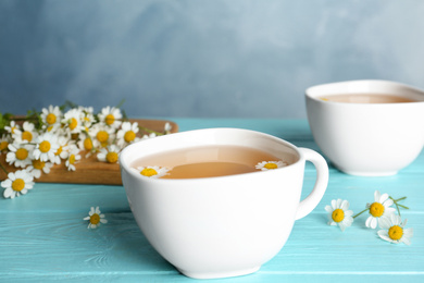 Fresh chamomile tea in cup on light blue wooden table