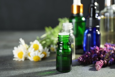 Photo of Bottles of essential oils and wildflowers on grey table, space for text