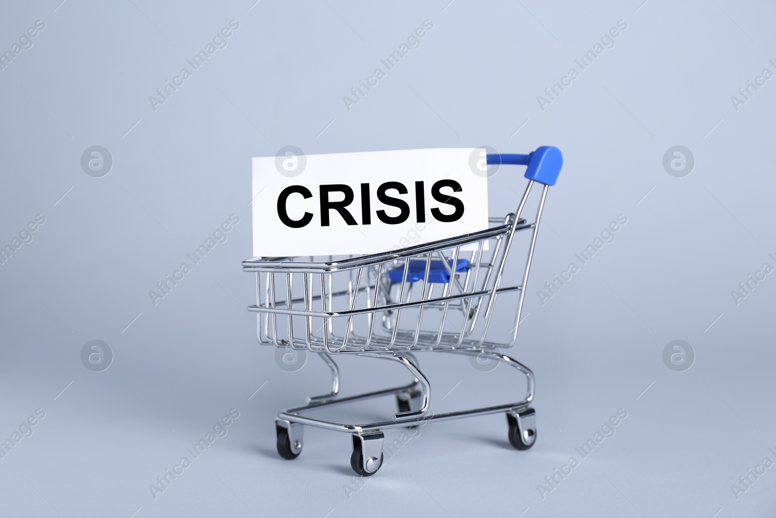 Photo of Mini metal cart and word Crisis on light background