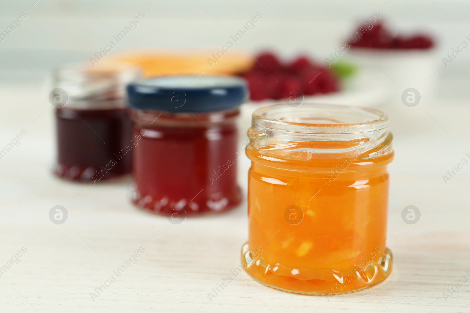 Photo of Jars with different sweet jams on white wooden table, closeup. Space for text