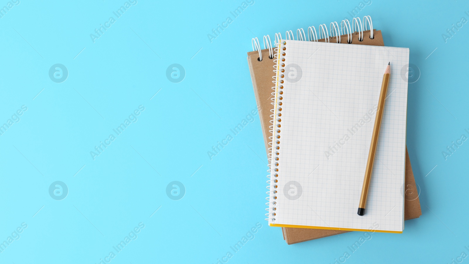 Photo of Notebooks with pencil on light blue background, top view. Space for text