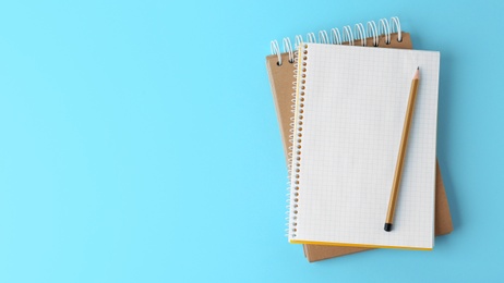 Photo of Notebooks with pencil on light blue background, top view. Space for text