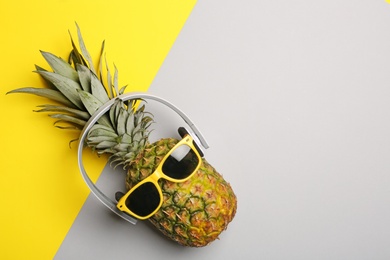Photo of Funny pineapple with headphones and sunglasses on color background, top view. Space for text
