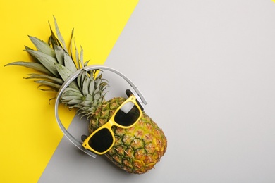 Funny pineapple with headphones and sunglasses on color background, top view. Space for text