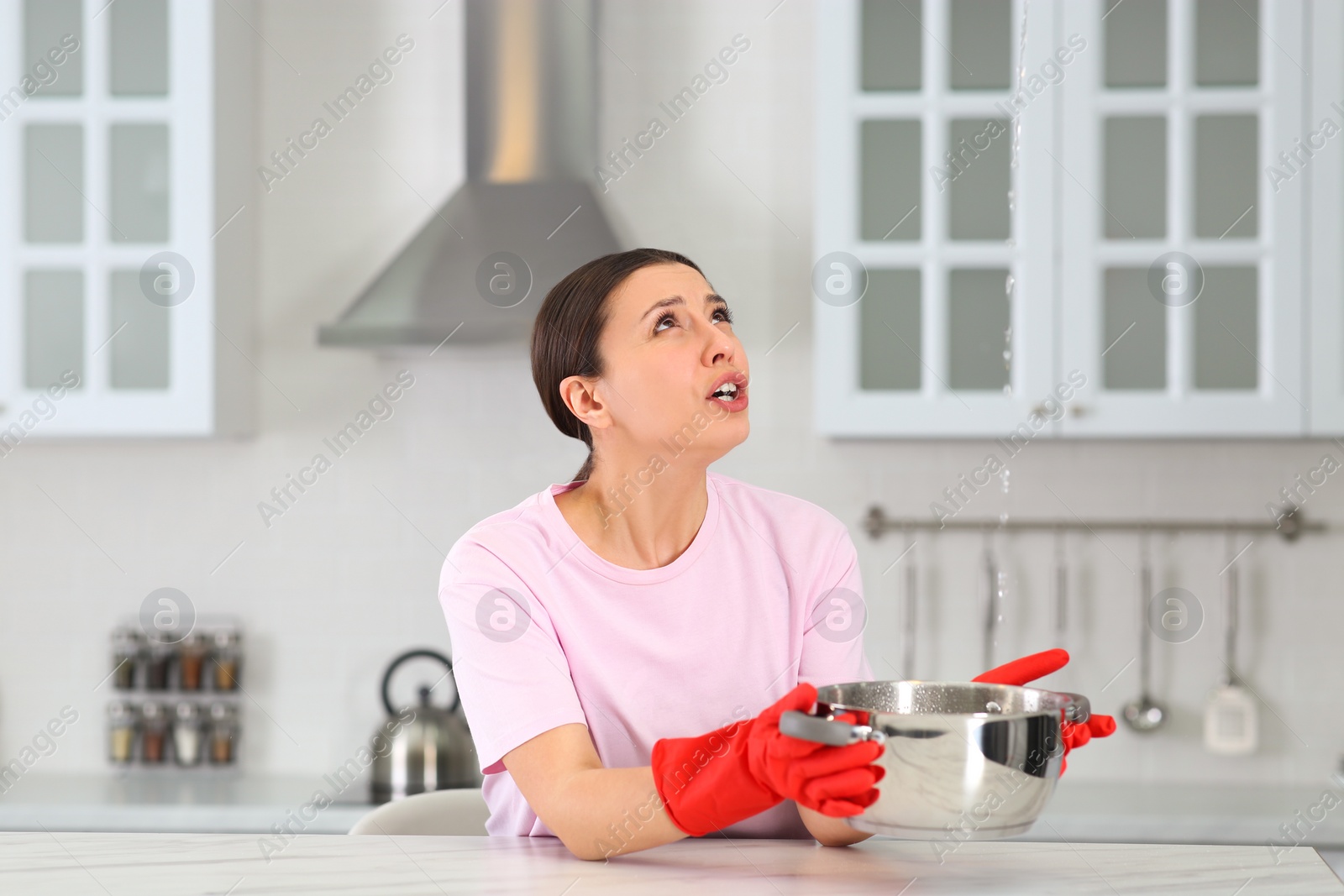 Photo of Young woman collecting leaking water from ceiling in kitchen. Time to call roof repair service