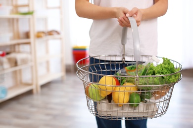 Photo of Woman with shopping basket full of products in grocery store, closeup