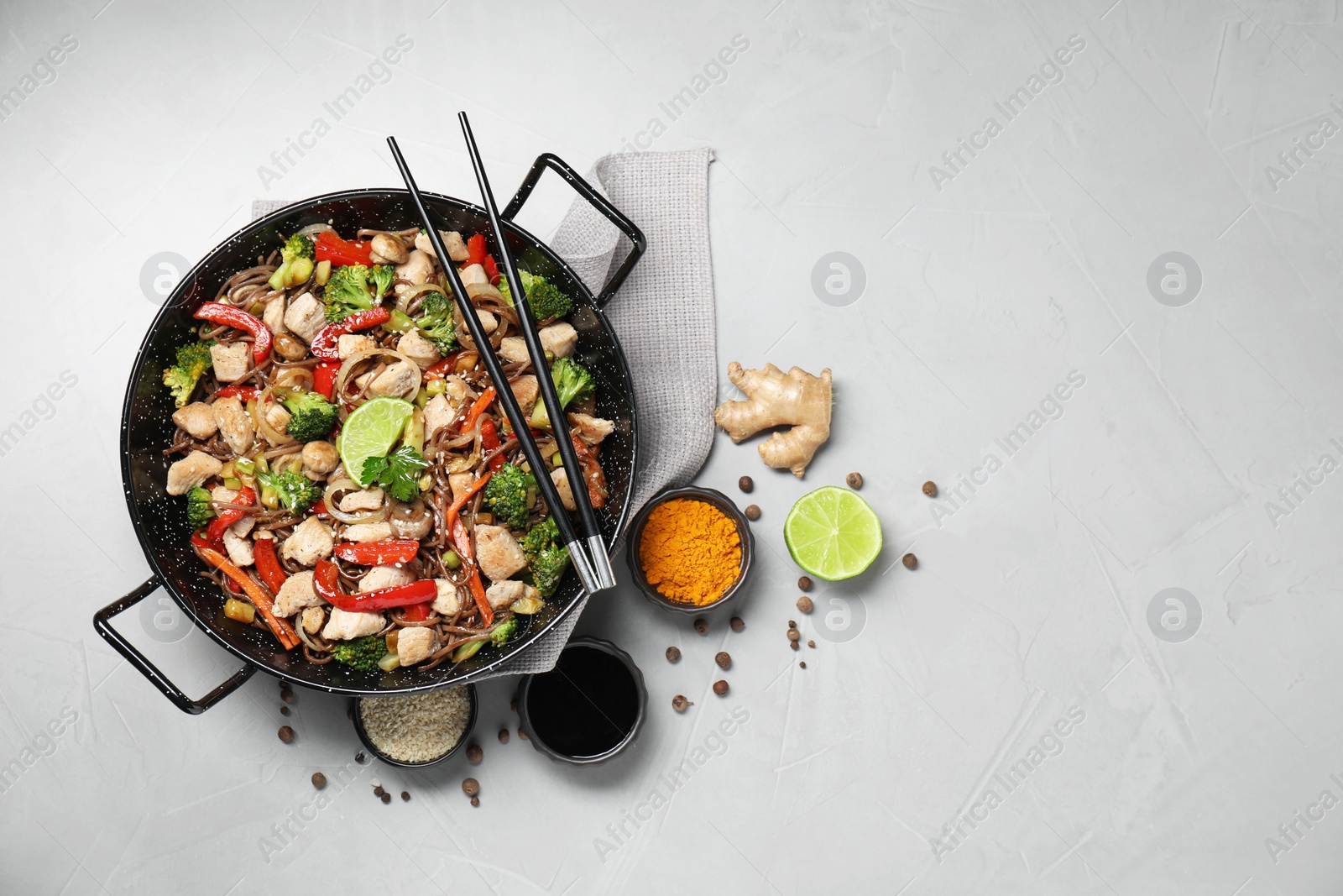 Photo of Stir-fry. Tasty noodles with meat in wok, chopsticks and ingredients on grey textured table, flat lay. Space for text