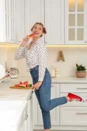 Beautiful teenage girl with slice of watermelon near countertop in kitchen