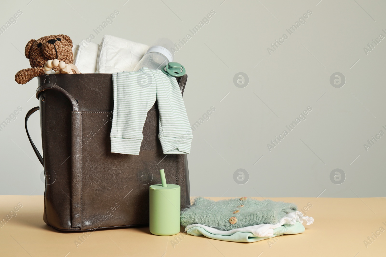 Photo of Mother's bag with baby's stuff on beige surface against grey background. Space for text