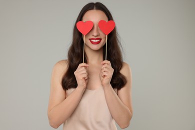 Young woman covering her eyes with paper hearts on grey background