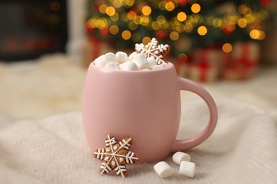 Photo of Christmas cocoa with marshmallows in pink cup on soft blanket indoors, closeup